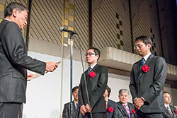 栗島聡ＪＤＭＣ会長より表彰状を授与される、同学　総合企画室　ＩＲ推進グループ　西出崇講師（中央）